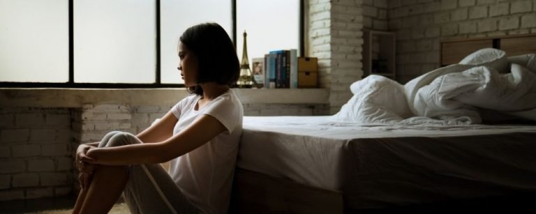 Eenzame vrouw die tegen haar bed aanzit terwijl ze haar benen vasthoudt