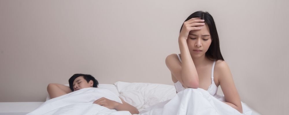 Vrouw zit op bed naast man en heeft geen zin in seks