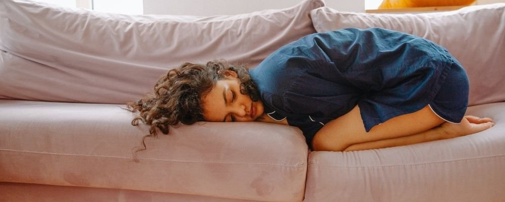Woman lying on the couch with her hands around her stomach and she is curled up